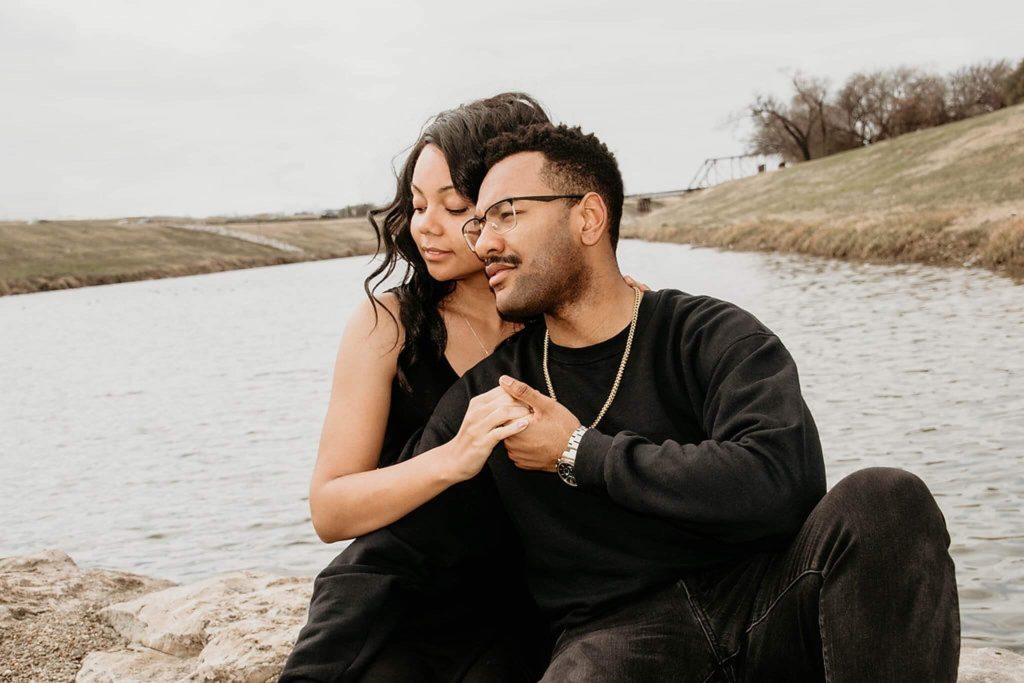 A couple sits with their arms around each other by the water representing a strong couple who has used Couples Therapy in Boca Raton, FL to their benefit.
