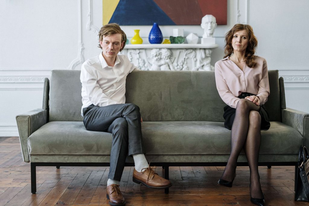 A couple sits apart on a couch not loking at each other representing a couple who could benefit from working with a Marriage Counselor in Boca Raton, FL.