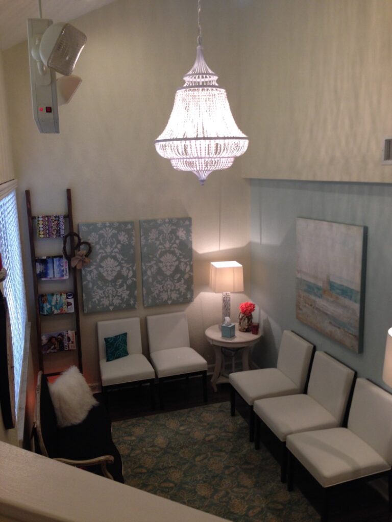 lobby space featuring a white beaded empire-style chandelier, white armchairs, and teal damask wall art
